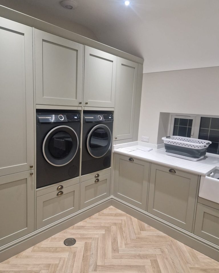 Modern laundry area with Sage Green cabinetry, stacked washer and dryer, pull out laundry shelves and a quartz worktops with upstands.